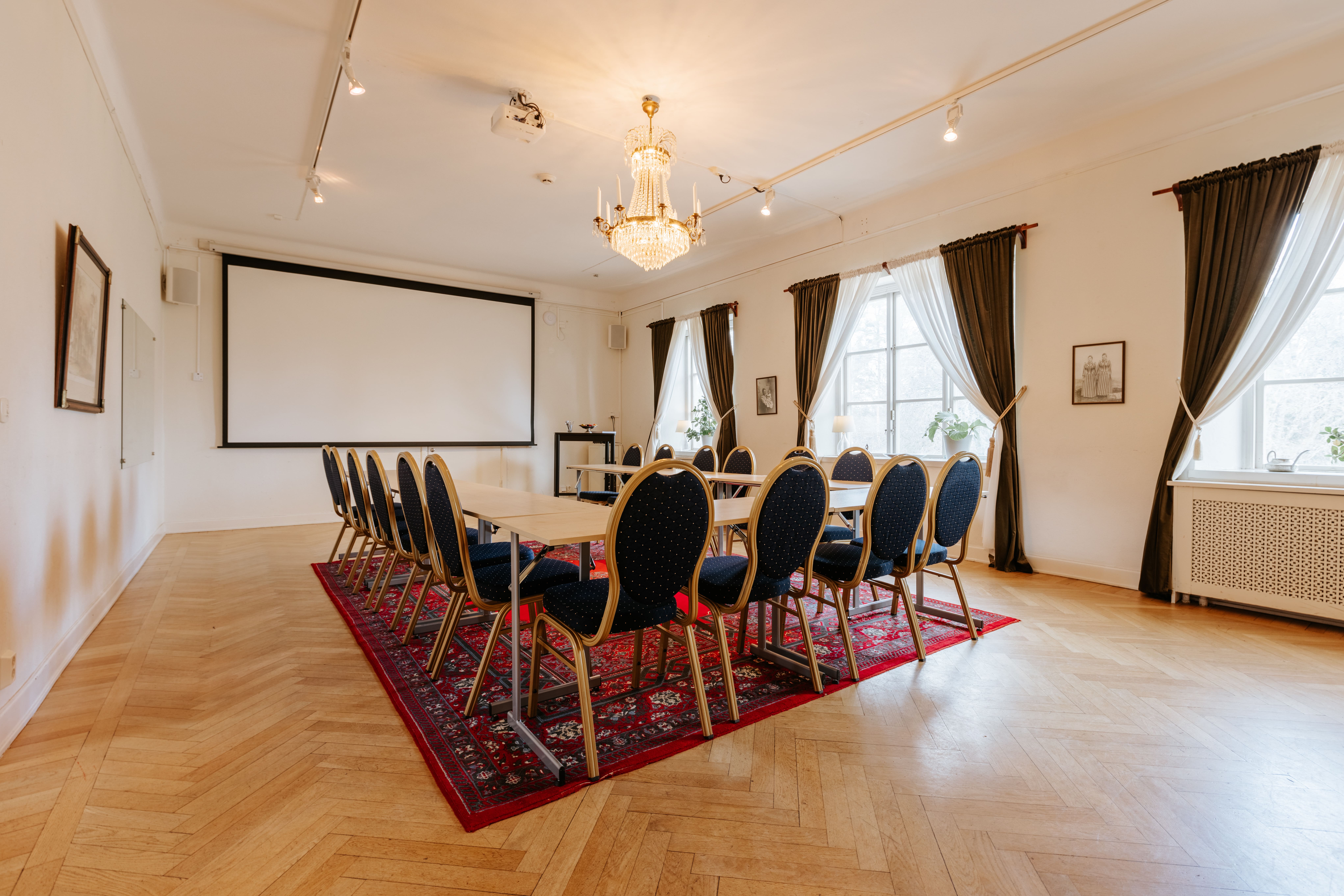 Konferensrum med rundbord, mörka stolar och ljus inredning, dekorerat med en matta och kristallkrona. Passande för gruvstigarens konferens.