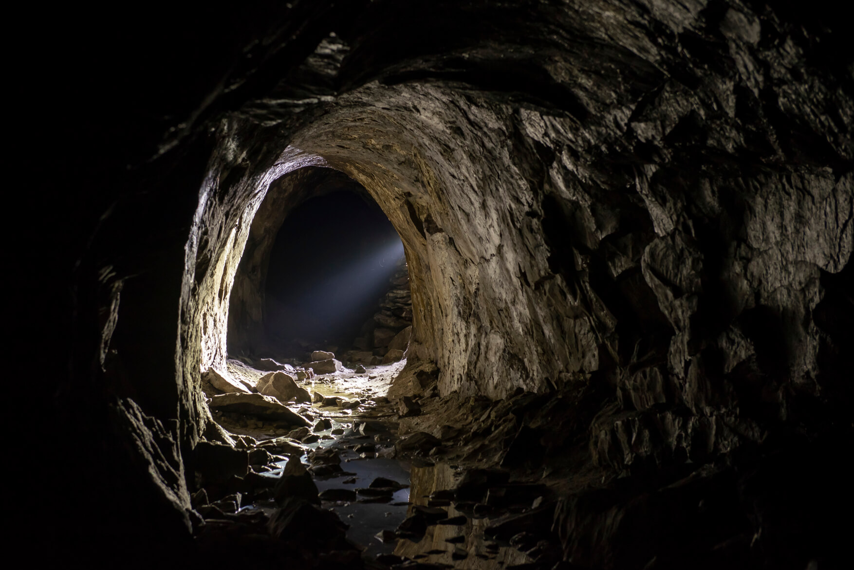 Underground mine tunnel in Sala Silvergruva with rugged rock walls and a distant arched passage opening