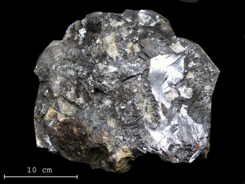 Blyglans från Sala Silvergruva, glänsande mineral med svart och silverfärgad yta, ligger på svart bakgrund.