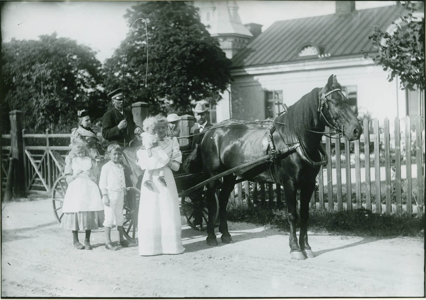 En familj med barn står vid en häst och vagn framför ett hus i Sala, 1891. Traditionellt gatuliv med historisk känsla.