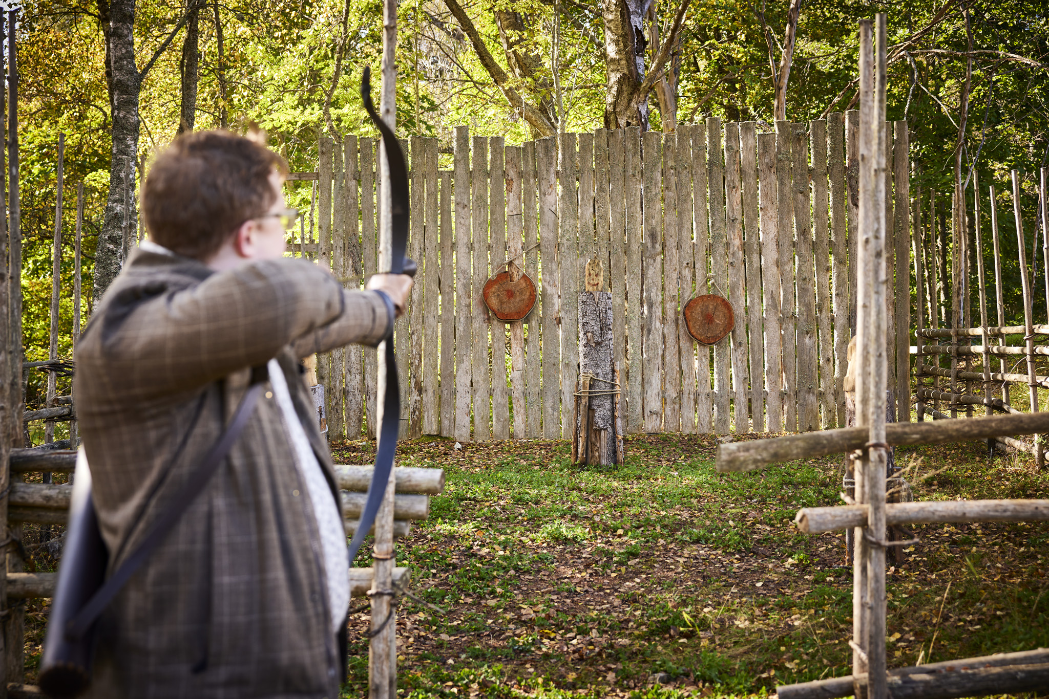 En man siktar med pilbåge mot två träplattor på en vägg i en grönskande miljö vid Sala Silvergruva.