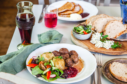 Traditionell svensk husmanskost med köttbullar, potatis, sås, lingonsylt och frisk grönsallad på en matdukad bordsyta.