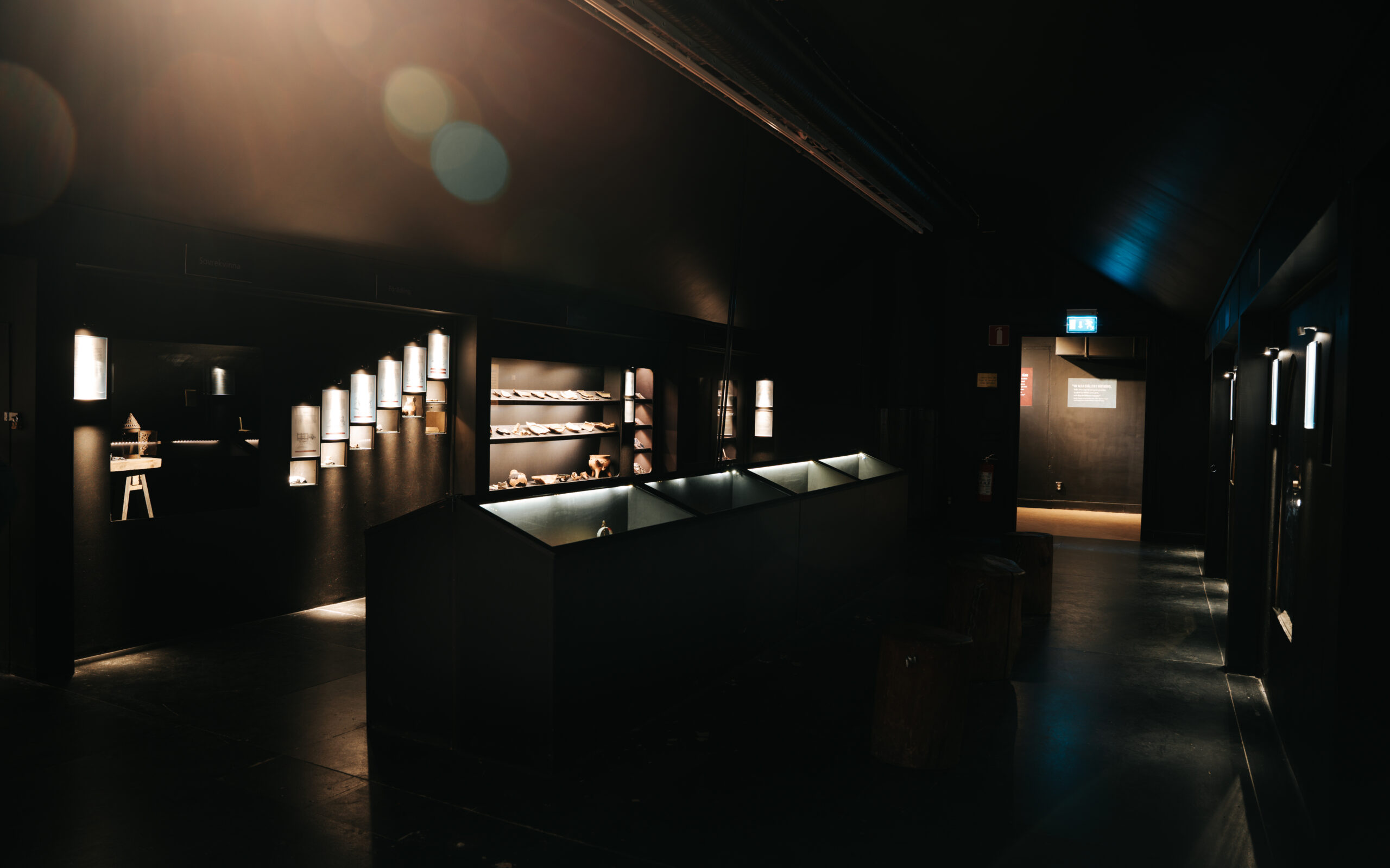 Modern exhibition space in a dimly lit mine with sleek displays showcasing artifacts and illuminated wall fixtures.