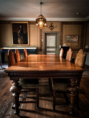 A wooden dining table surrounded by chairs, illuminated by a geometric pendant light, set in an elegant room with rich decor.