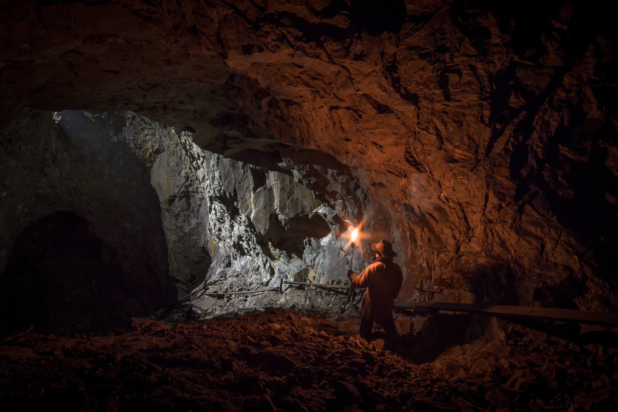 A miner stands in a dimly lit tunnel, holding a torch that illuminates rocky walls and the underground environment.